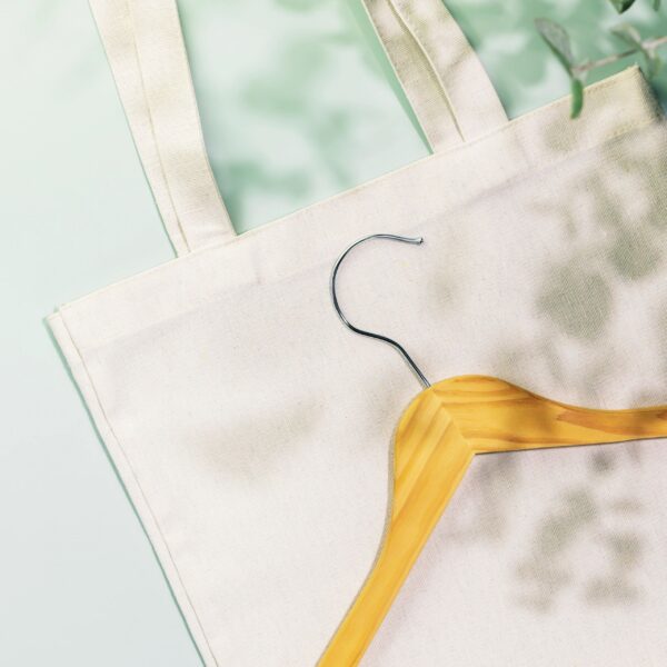 Wooden hanger on textile shopping bag on blue background